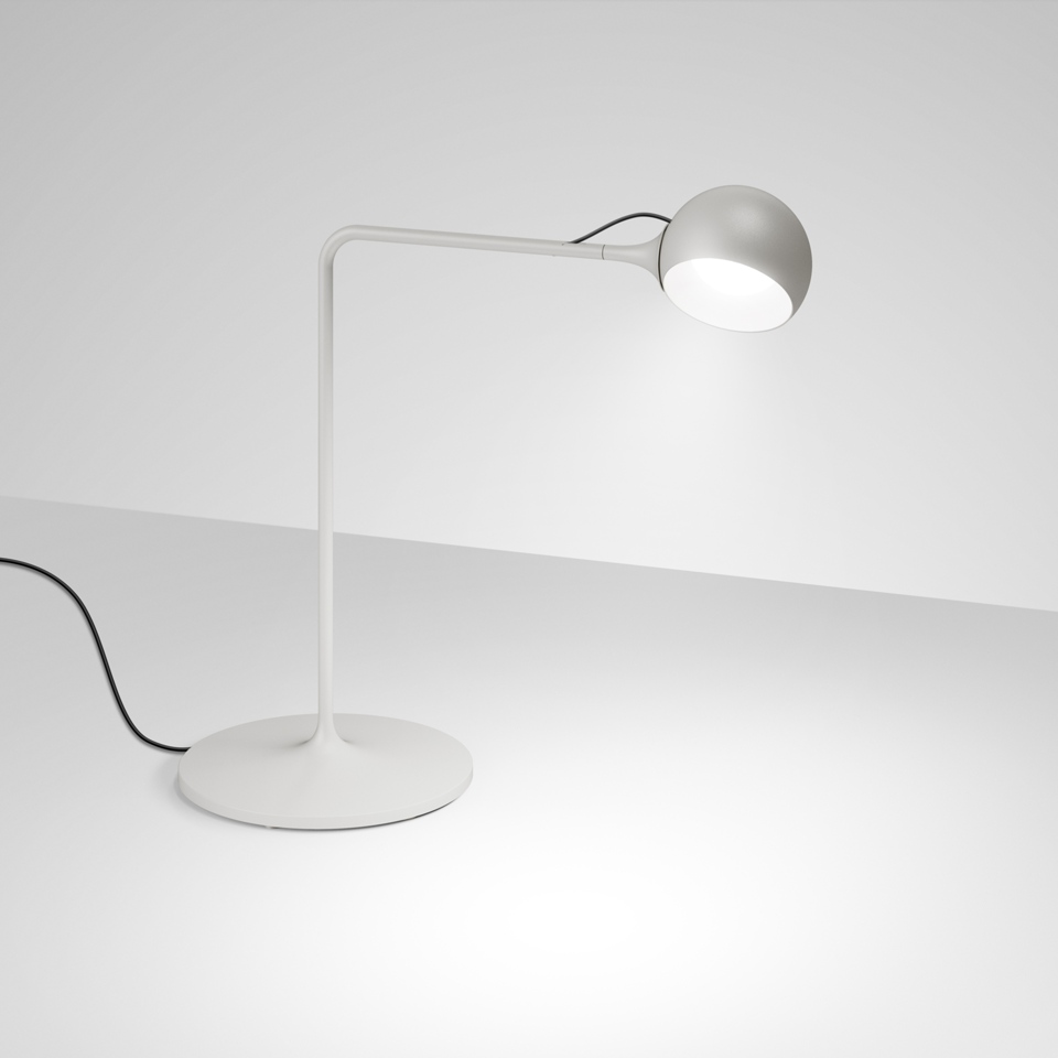 Artemide Ixa table lamp in white with articulated arm, spherical metallic shade, and circular base, emitting focused warm light