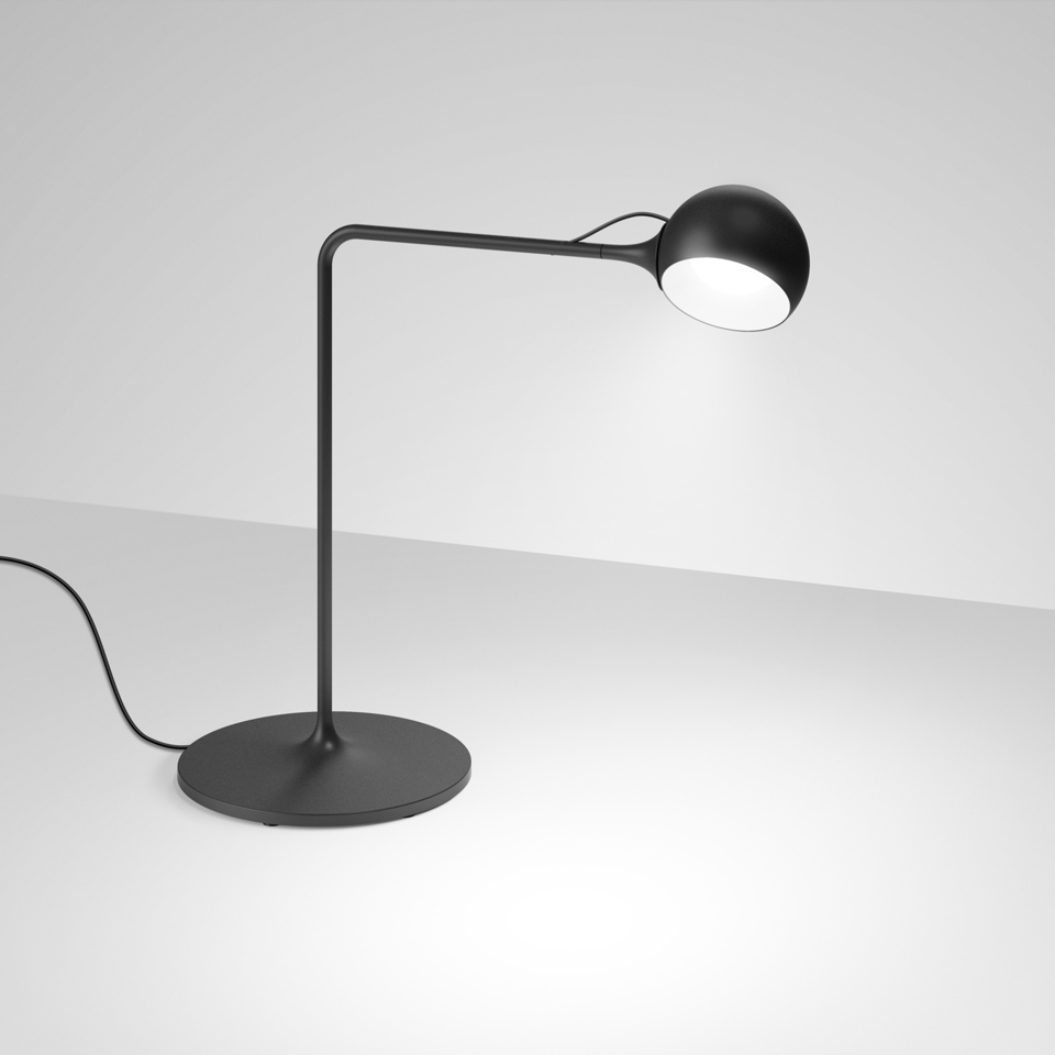 Artemide Ixa table lamp in black with round base, curved arm, and adjustable spherical head emitting focused white light