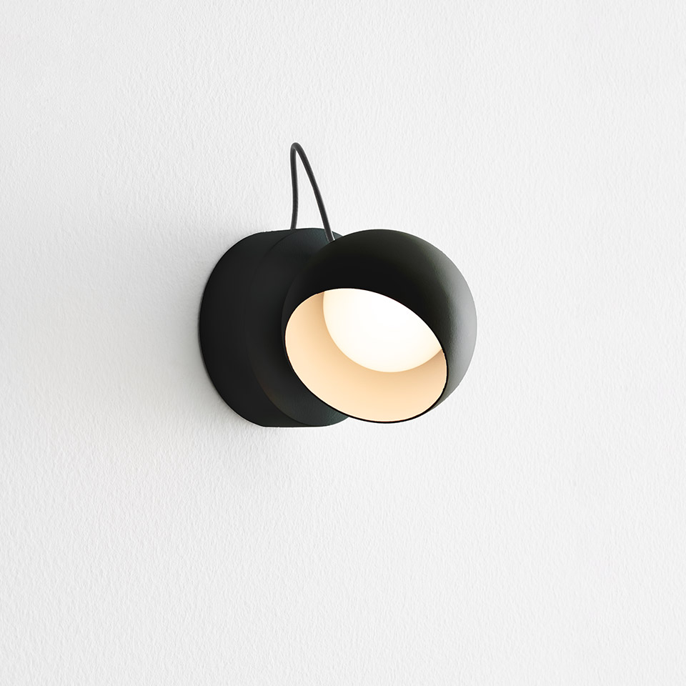 Artemide Ixa wall lamp in matte black, featuring a rotating spherical shade revealing warm white interior light