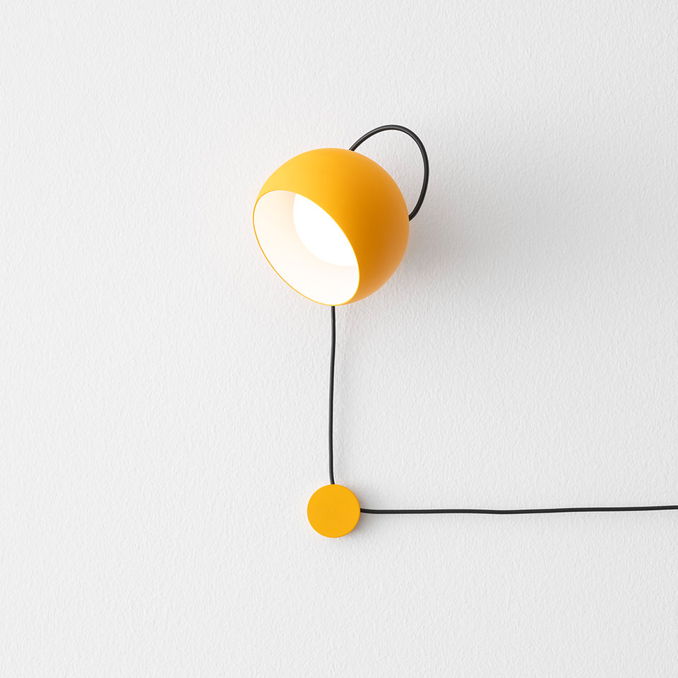 Artemide Ixa wall lamp: yellow spherical shade on black wire arc, directional light, with yellow circular dimmer switch below