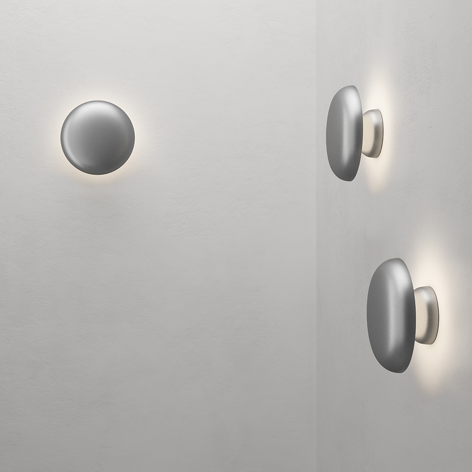 Artemide Knop wall lamps: round disc-shaped aluminum fixtures mounted on wall, emitting soft indirect halo light around edges