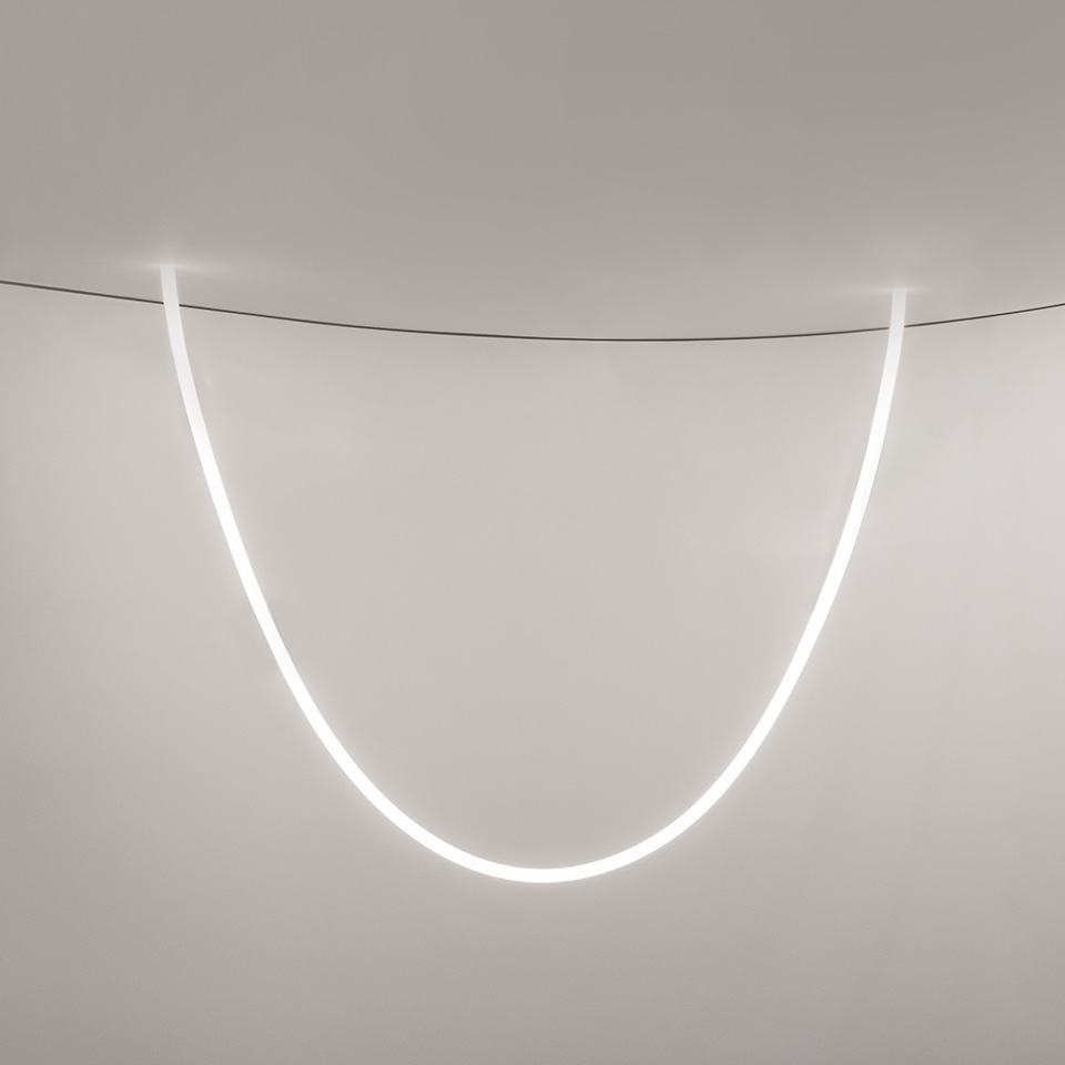 Artemide La Linea pendant light: a glowing flexible LED tube suspended in a graceful U-shaped curve from the ceiling