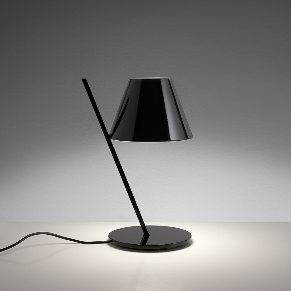 Artemide La Petite table lamp in black: diagonal stem on round base, conical glossy shade directing warm downward light