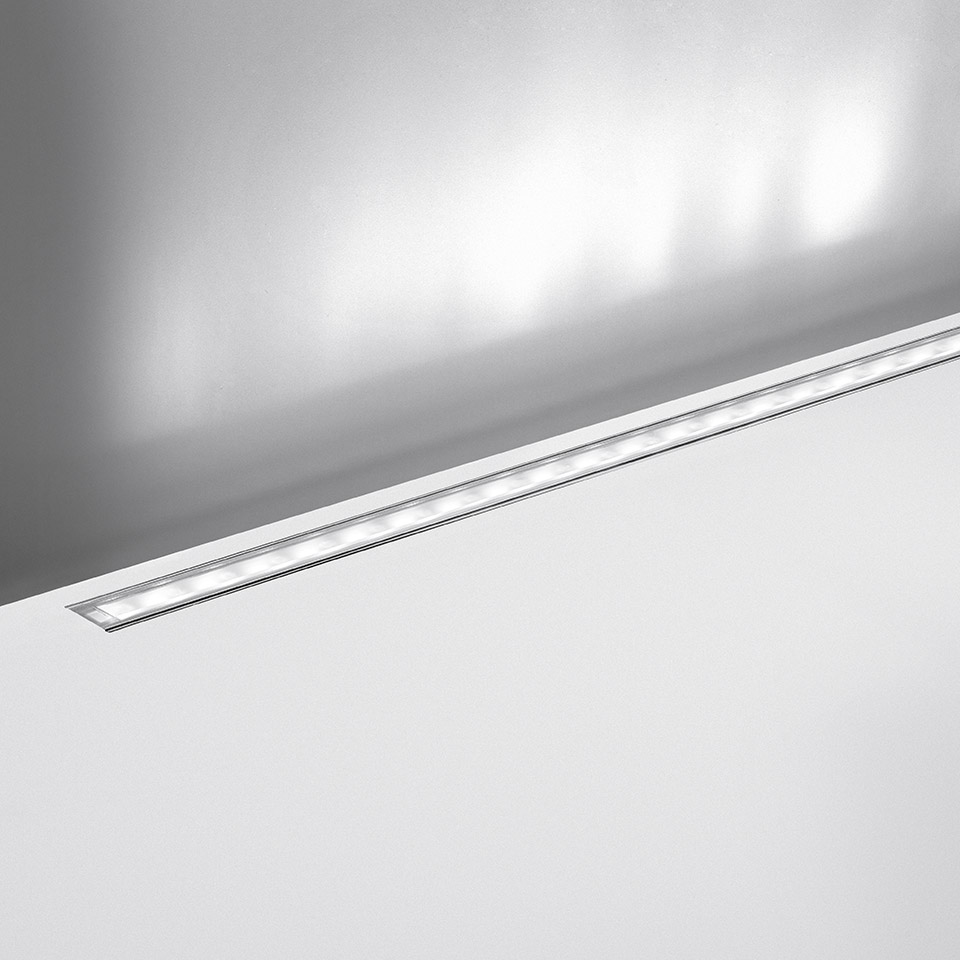 Artemide LineaLed Wallwasher: slim recessed LED linear fixture flush-mounted in white ceiling, projecting soft upward light on wall