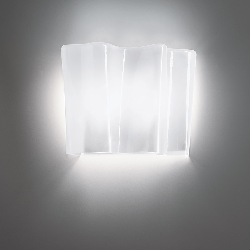 Artemide Logico wall lamp with layered frosted glass diffuser emitting soft white light, creating a glowing halo on the wall