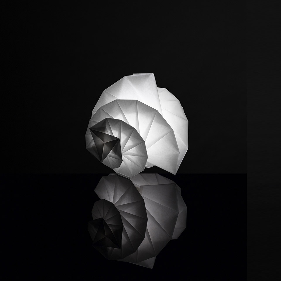 Artemide In-Ei Mendori by Issey Miyake: glowing origami-inspired spiral shell-shaped table lamp in white, reflected on black surface
