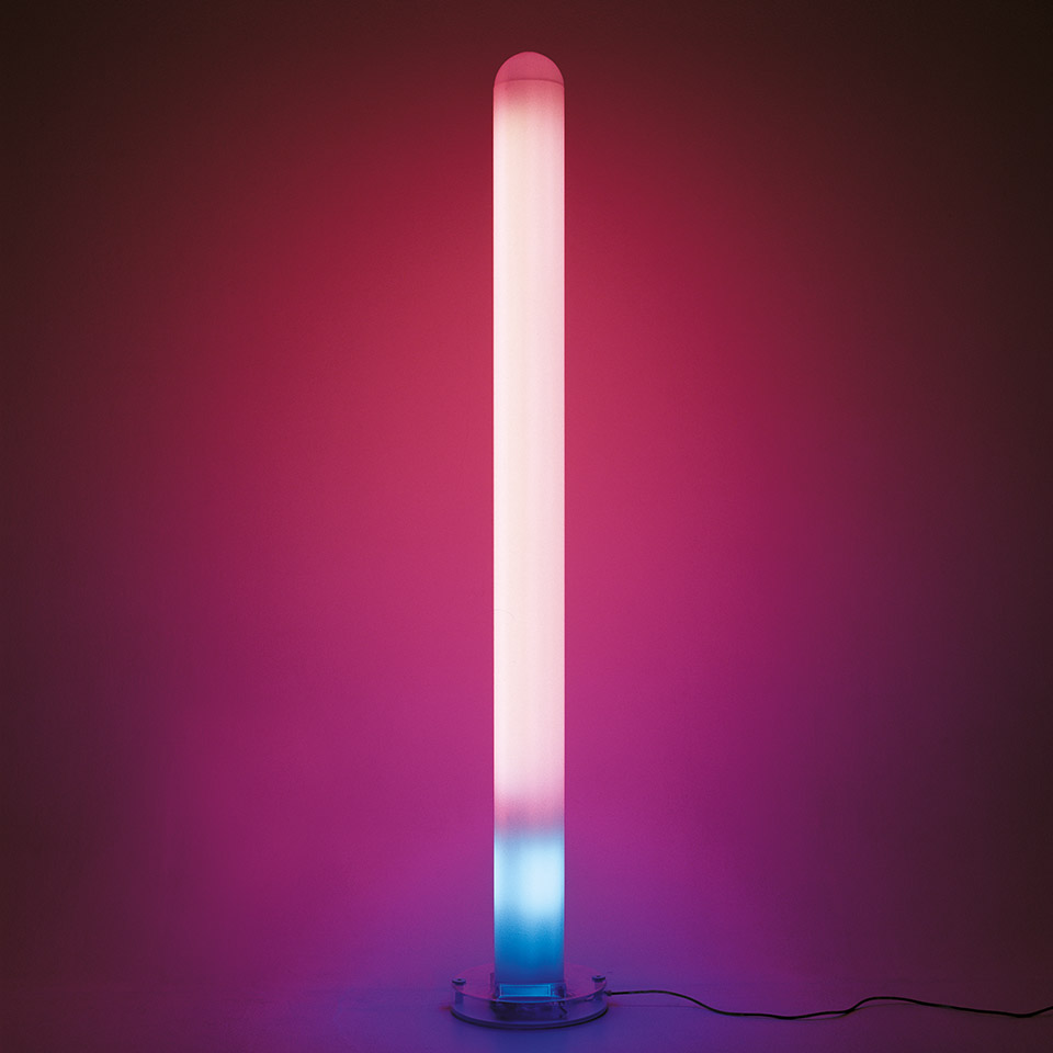 Artemide Metacolor floor lamp: tall cylindrical diffuser emitting gradient light from pink-white at top to cyan-blue at base, on round transparent base
