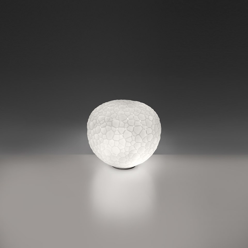 Artemide Meteorite Tavolo table lamp: glowing spherical white glass diffuser with organic cellular texture, resting on a small base