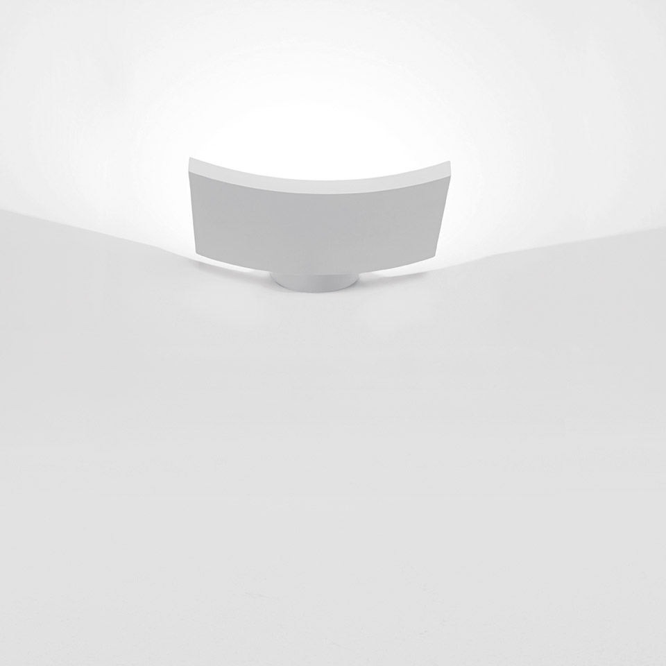 Artemide Microsurf white wall light mounted at wall-ceiling corner, emitting soft upward indirect light glow