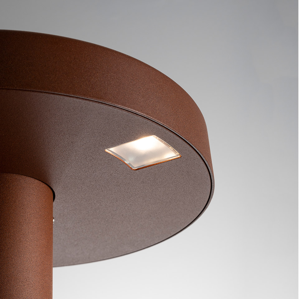 Close-up of Artemide Needoo outdoor bollard light in rust brown finish, featuring a square frosted LED lens on the circular top cap