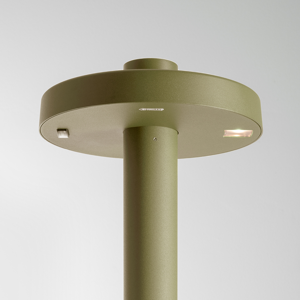 Artemide Needoo table lamp close-up: olive green cylindrical stem with flat circular disc head featuring integrated LED light