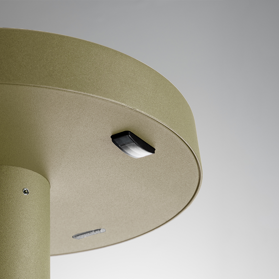 Close-up of Artemide Needoo outdoor lamp base in gold finish, showing black LED module and ventilation slot on circular housing