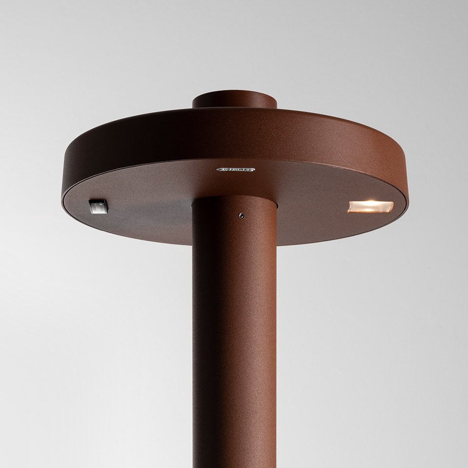 Artemide Needoo outdoor floor lamp, close-up of rust-brown cylindrical stem with circular disc head and integrated LED light