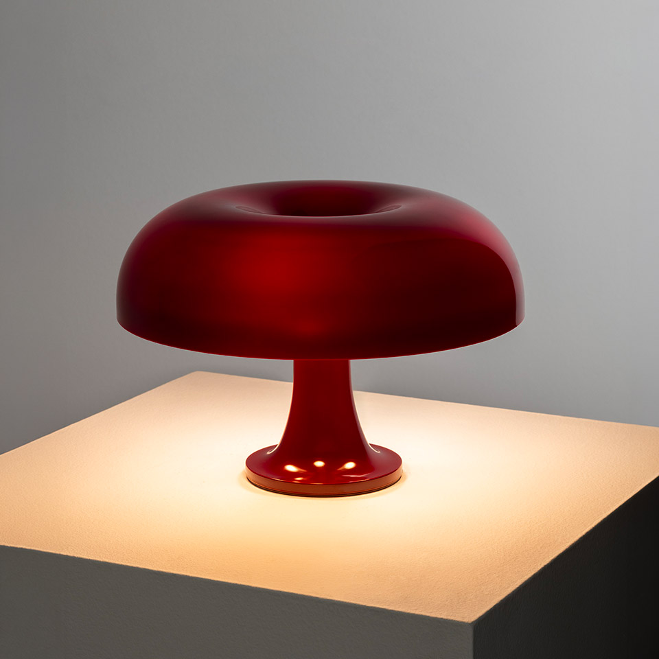 Artemide Nessino table lamp in red, featuring iconic donut-shaped diffuser on a slender stem base, casting warm light - 2