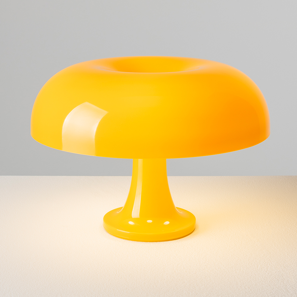 Artemide Nessino table lamp in vibrant yellow, featuring a rounded mushroom-shaped shade and pedestal base, glowing warmly on a surface - 2