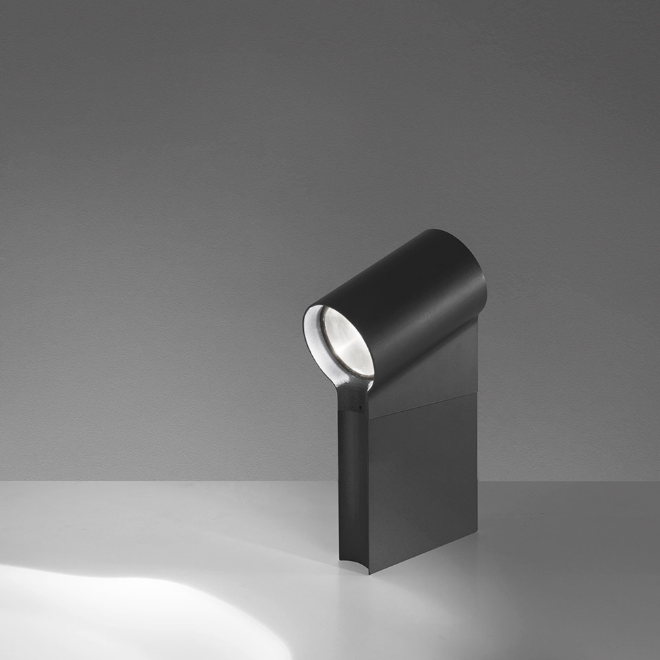Artemide Oblique table lamp in black, cylindrical head tilted forward on a flat base, projecting a focused beam of light