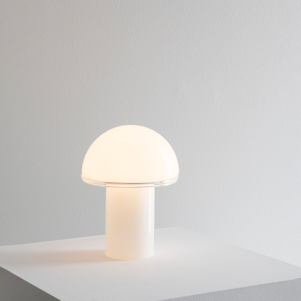 Artemide Onfale table lamp with mushroom-shaped opal white glass diffuser on a cylindrical base, softly glowing on a white surface
