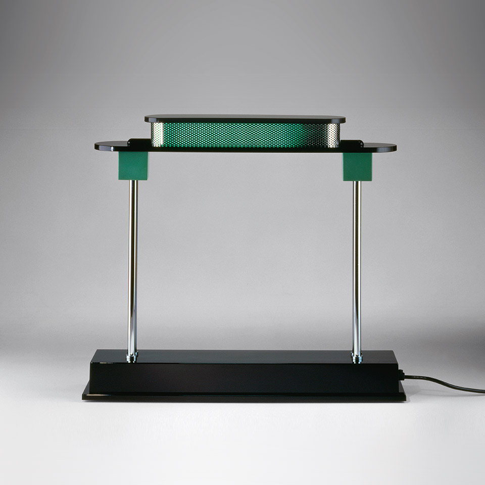 Artemide Pausania table lamp: black rectangular base, chrome vertical rods, green accents, perforated diffuser emitting warm light