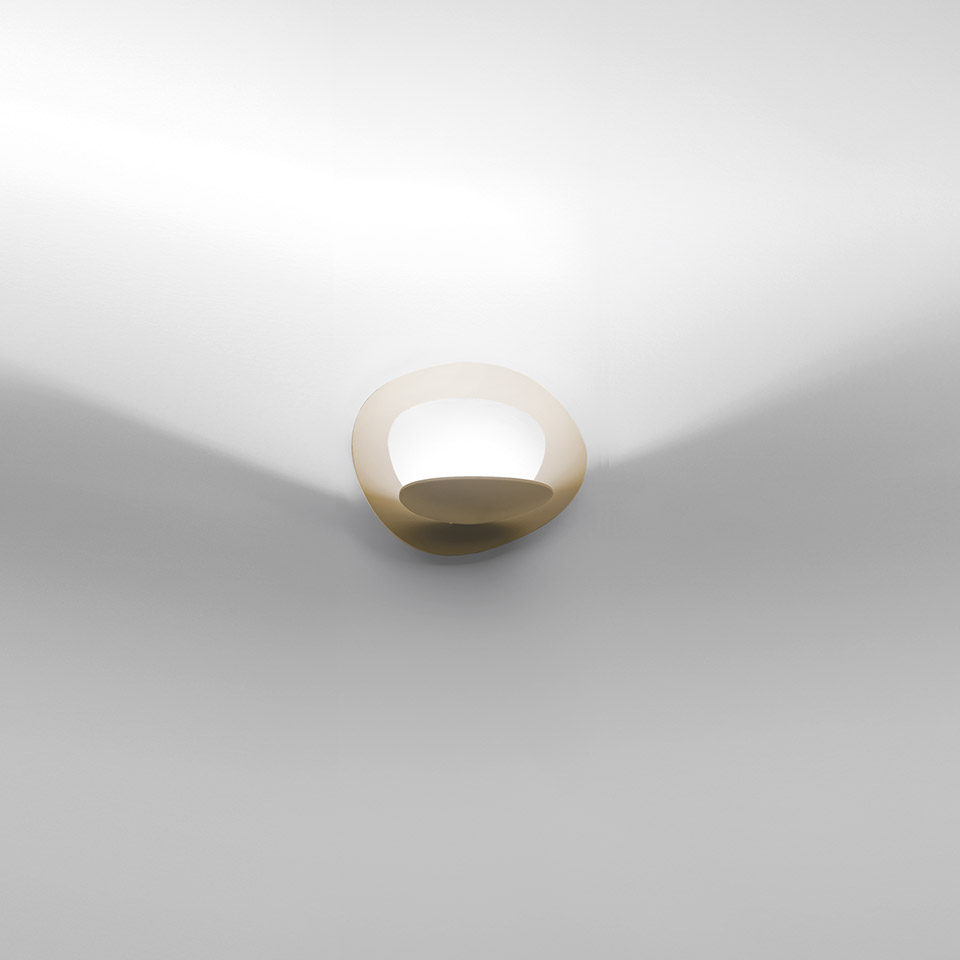 Artemide Pirce Parete wall lamp: golden dome-shaped diffuser mounted at wall-ceiling junction, casting soft upward and downward light