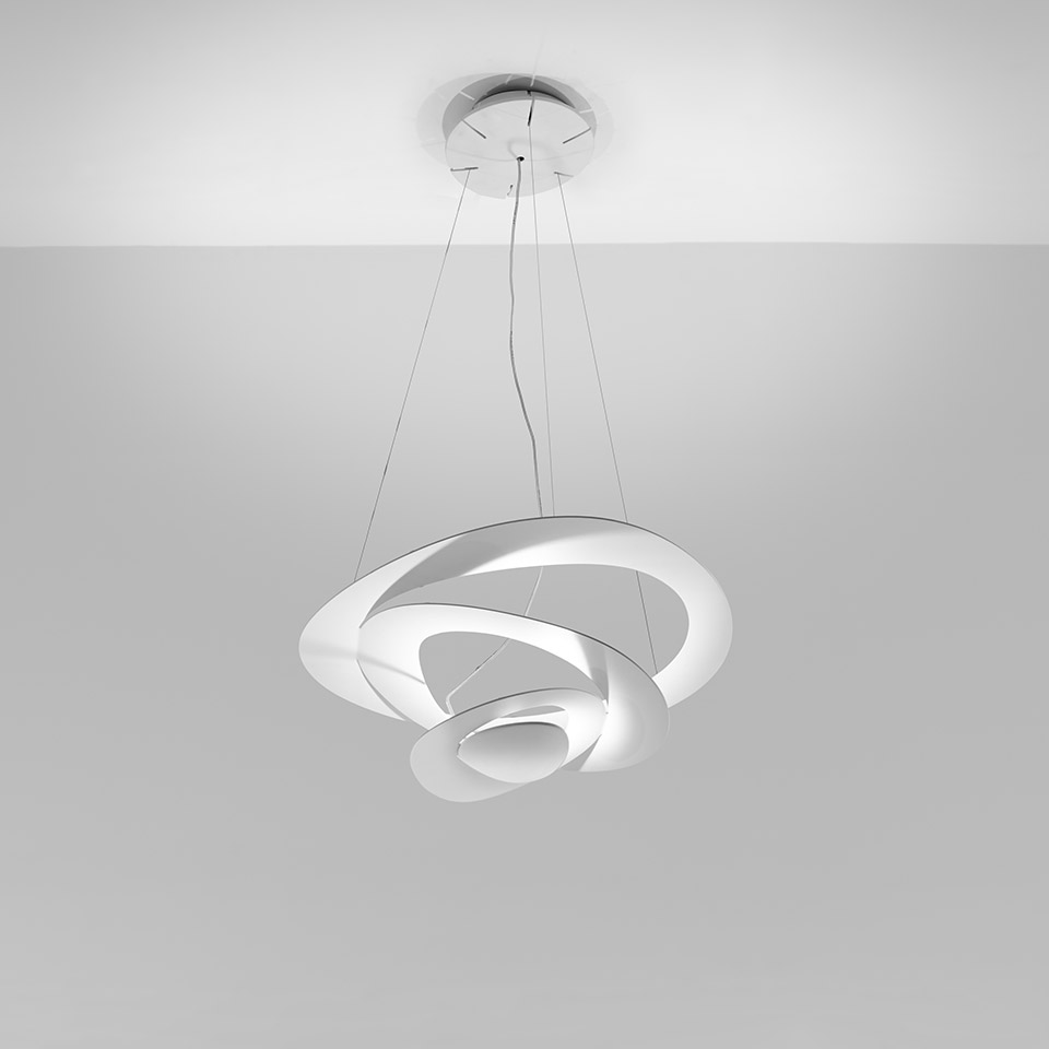 Artemide Pirce pendant lamp in white, featuring interlocking spiral rings emitting indirect light, suspended from ceiling by thin cables