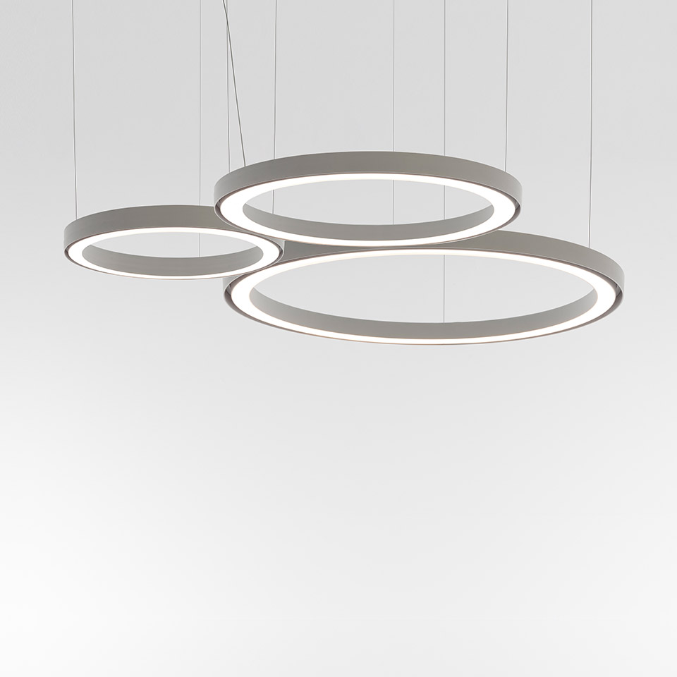 Three Artemide Ripple pendant lights: circular LED rings in grey, suspended at varying heights, sizes small, medium, and large