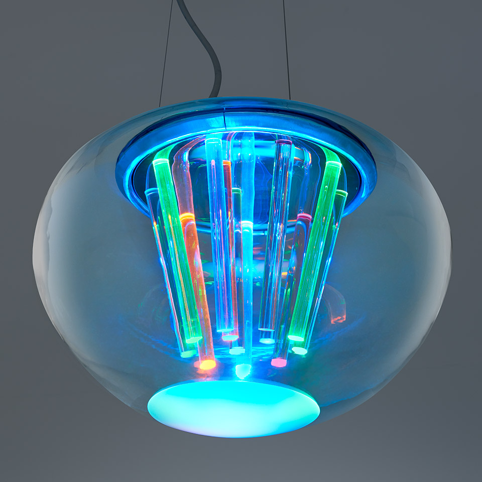 Artemide Spectral Light pendant lamp: transparent blue glass globe housing multicolored LED tubes emitting vibrant cyan, green, and orange light