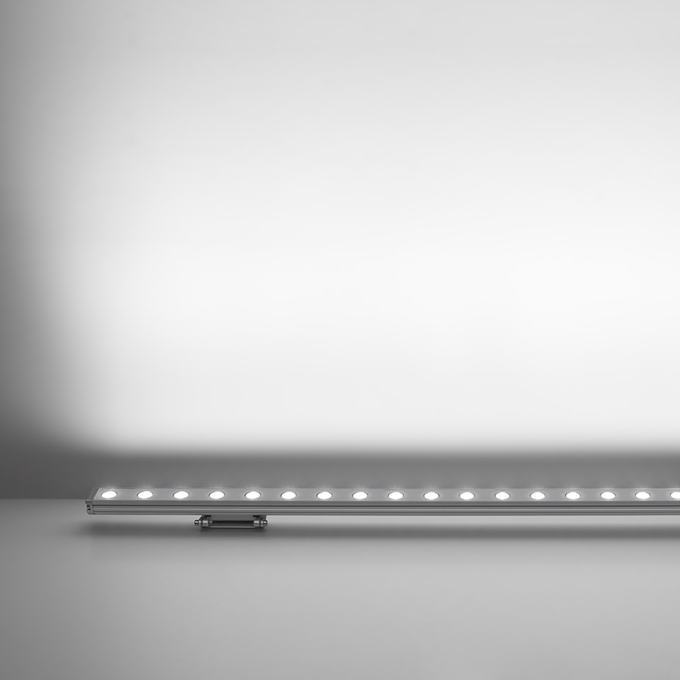 Artemide Spike linear LED bar in anodized aluminum, emitting uniform white light upward against a wall surface