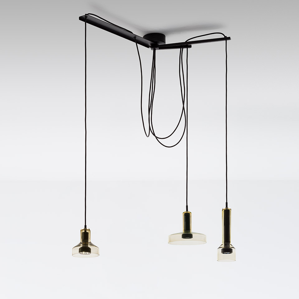 Artemide Stablight: three pendant lights with amber glass shades and brass fittings, suspended at varying heights from a black ceiling canopy with looped black cords