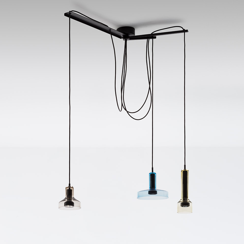 Artemide Stablight: three pendant lights on black cords from ceiling bar, featuring smoke, blue, and amber glass cylindrical shades