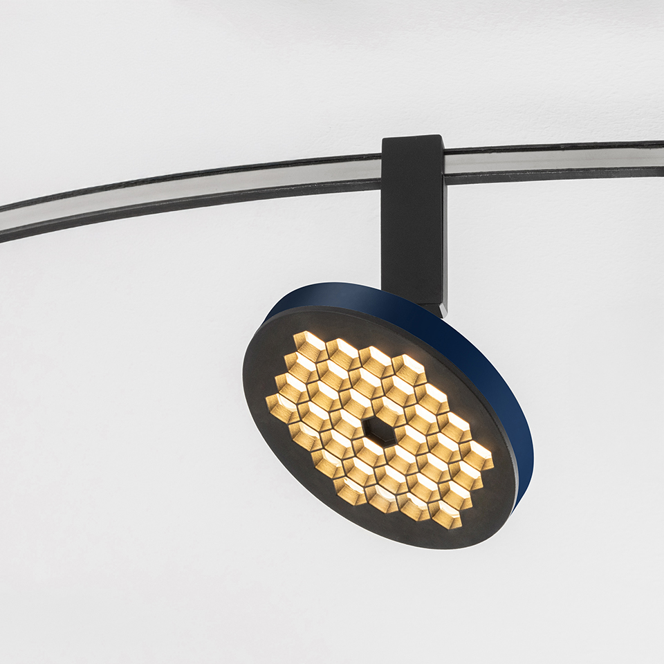 Artemide Sylt track spotlight with circular blue and black head featuring honeycomb LED array, mounted on curved black rail