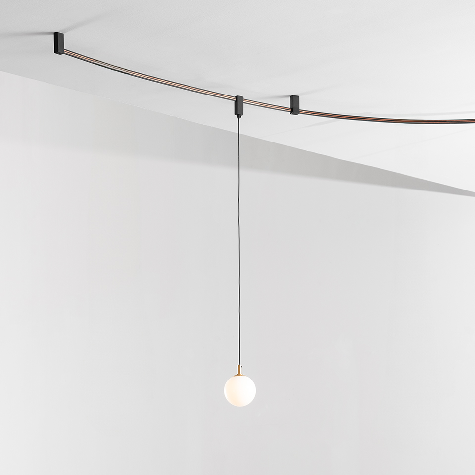 Artemide Sylt pendant lamp: opal glass sphere with brass detail hanging from a black cord on a curved ceiling-mounted cable system