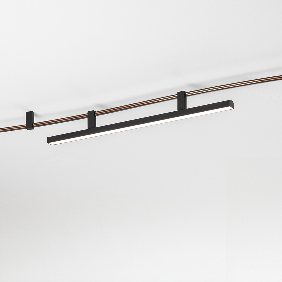 Artemide Sylt linear LED track light in matte black, mounted on a two-rail copper and black ceiling track system