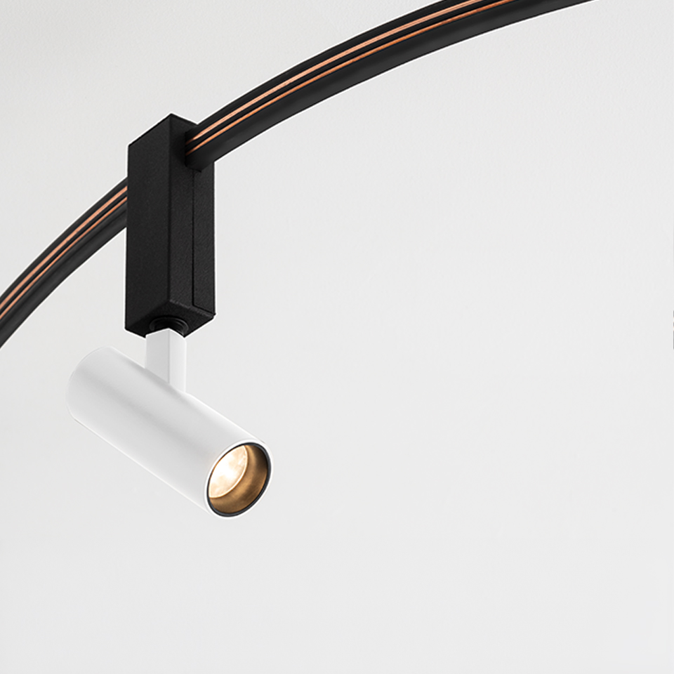 Artemide Sylt track spotlight: white cylindrical LED head on black rectangular adapter mounted on curved black rail with orange wiring