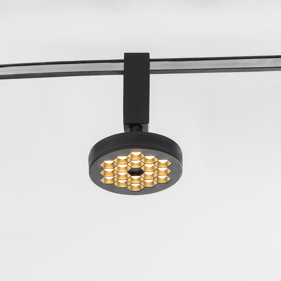 Artemide Sylt track spotlight in black with circular head featuring gold honeycomb LED array, mounted on ceiling rail