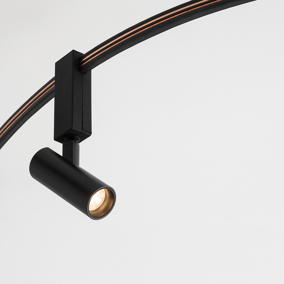 Artemide Sylt track spotlight in matte black, cylindrical head with warm LED, mounted on curved black and copper rail
