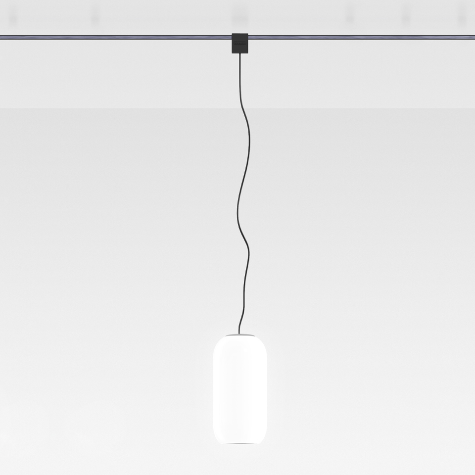 Artemide Sylt pendant lamp: oval white opal glass diffuser suspended by black cord from a dark track-mounted ceiling canopy