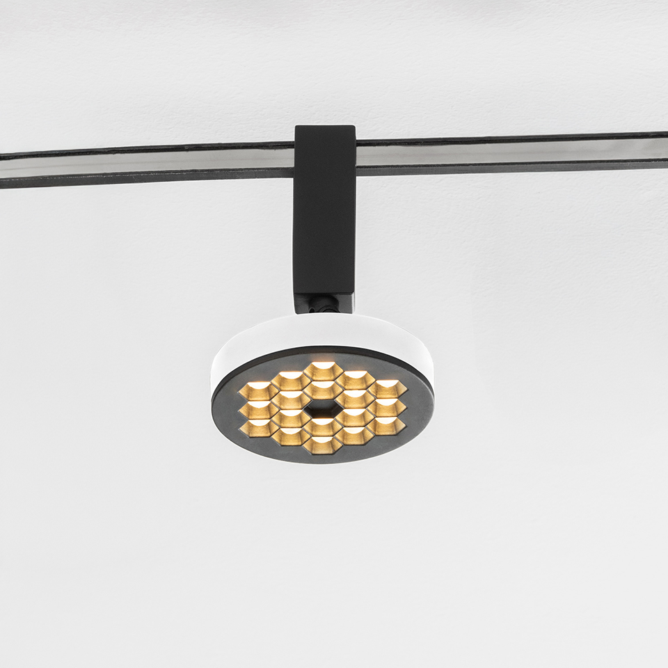 Artemide Sylt track spotlight with round white body, black honeycomb anti-glare grid, and gold LED array, mounted on black rail