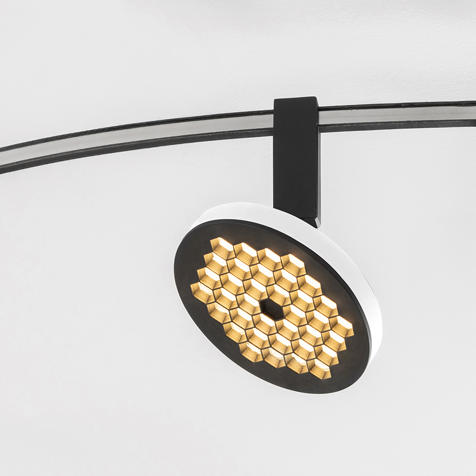 Artemide Sylt track spotlight with circular white and black head featuring honeycomb gold LED array, mounted on curved black rail