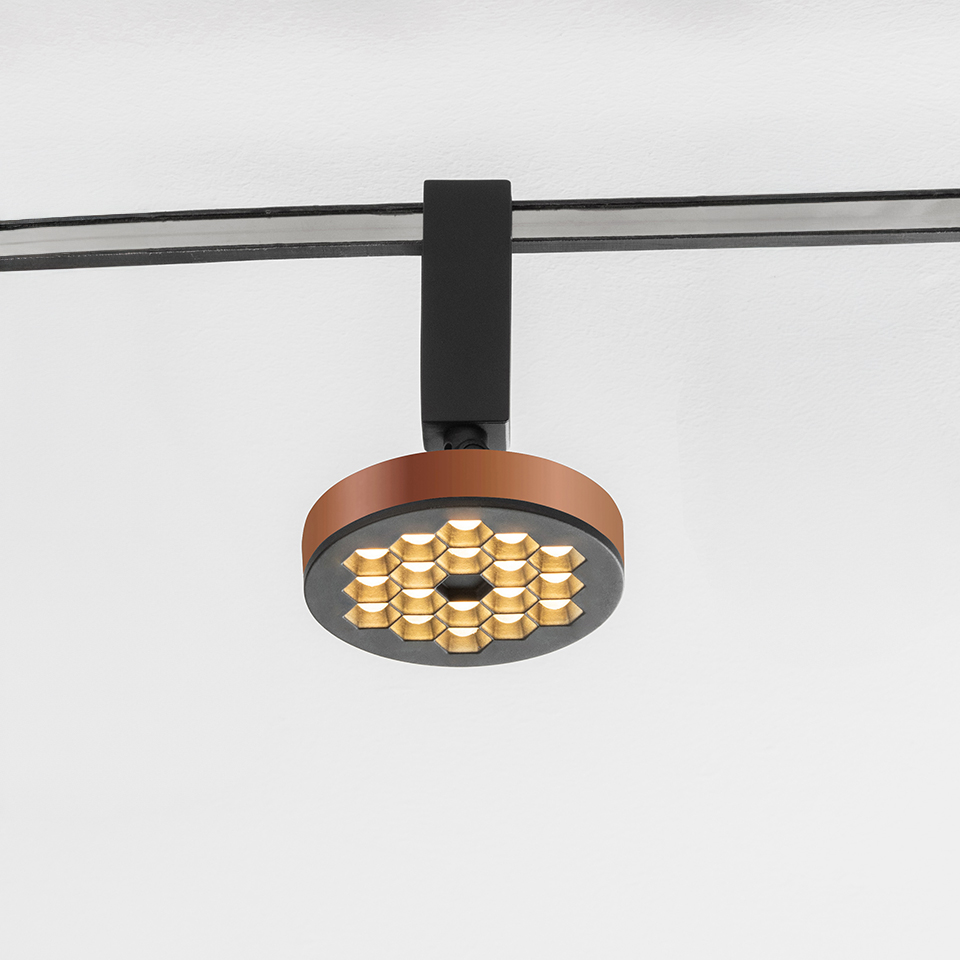 Artemide Sylt track spotlight with circular copper-tone body, honeycomb gold LED array, mounted on black rail system
