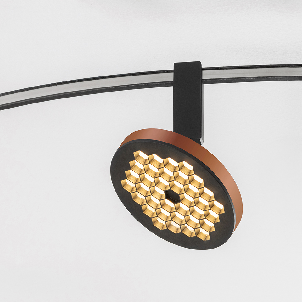 Artemide Sylt track spotlight with circular black and copper head featuring honeycomb LED array, mounted on curved black rail
