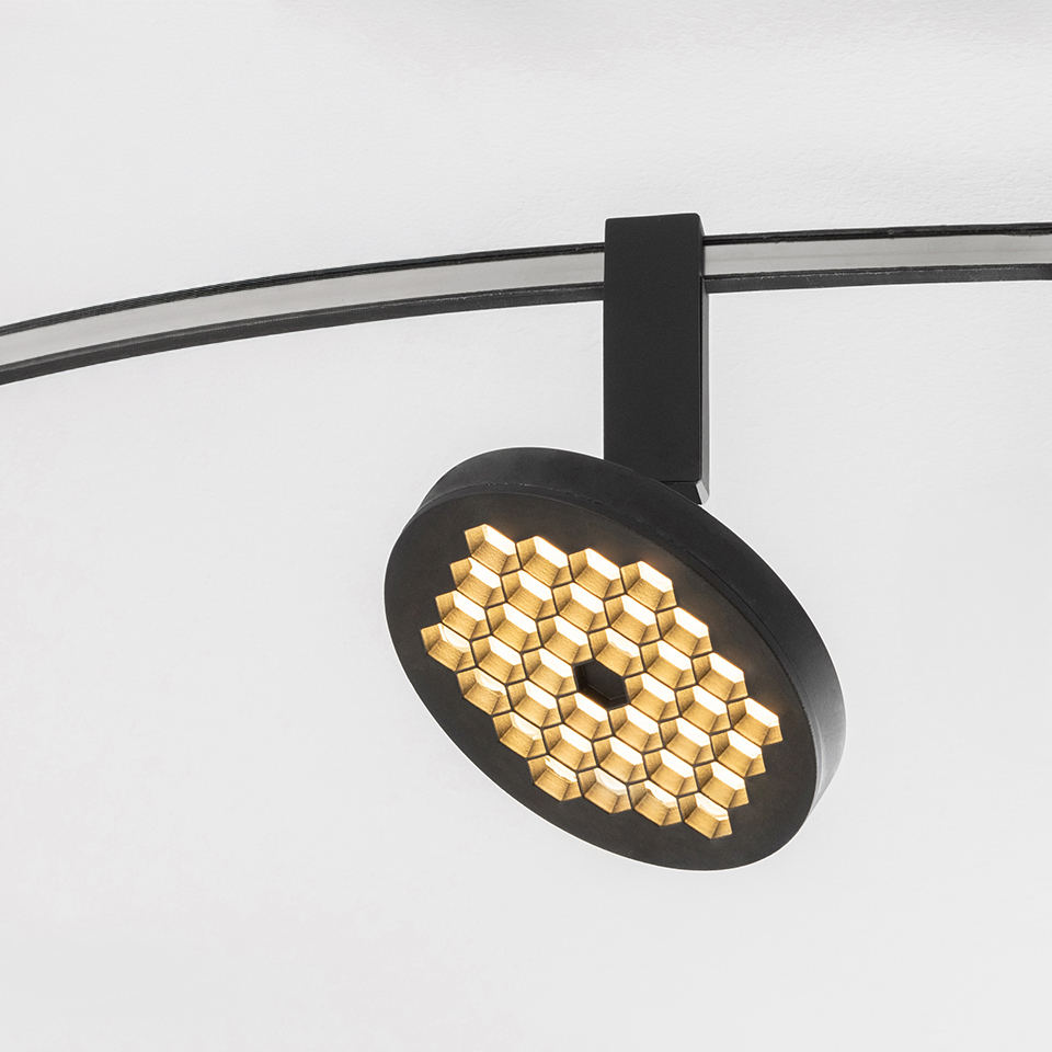 Artemide Sylt track spotlight in matte black with circular head featuring honeycomb LED array, mounted on curved ceiling rail