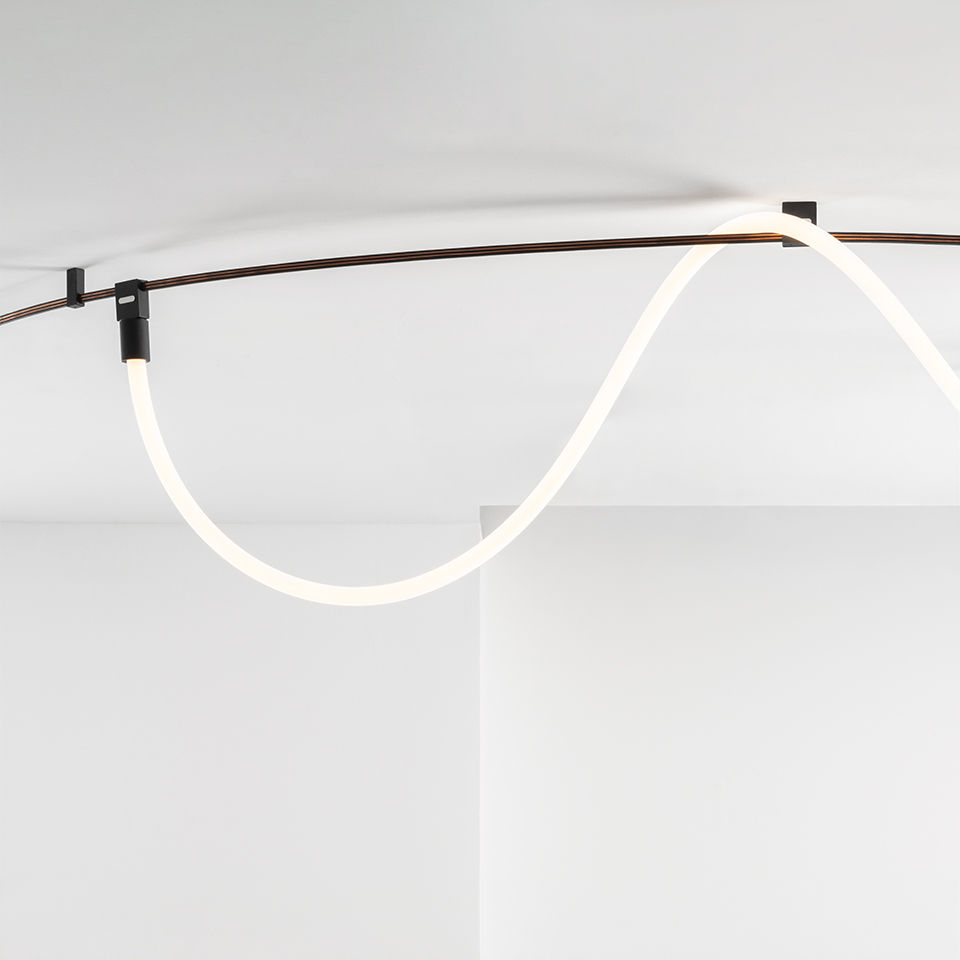 Artemide Sylt ceiling lamp: flexible glowing white LED tube forming a wave, mounted on ceiling with dark metal brackets