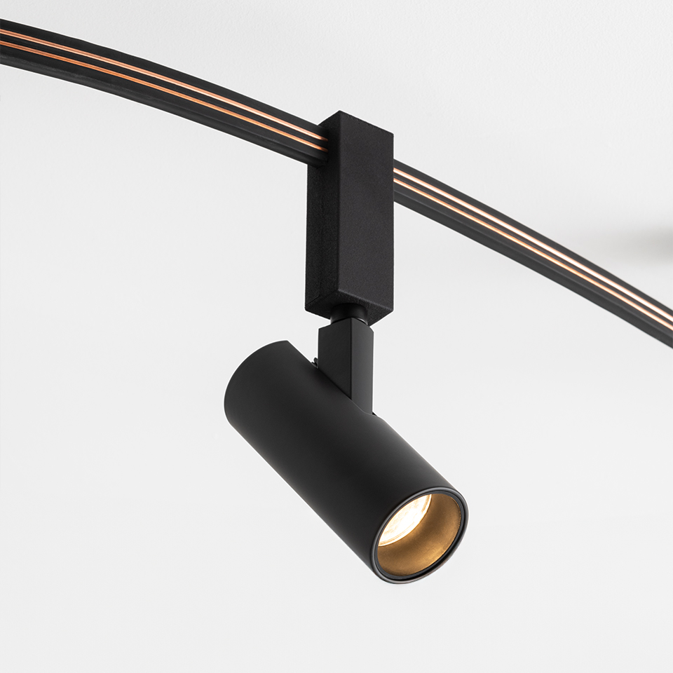 Artemide Sylt track spotlight in matte black, cylindrical head with gold interior, mounted on a curved black rail system