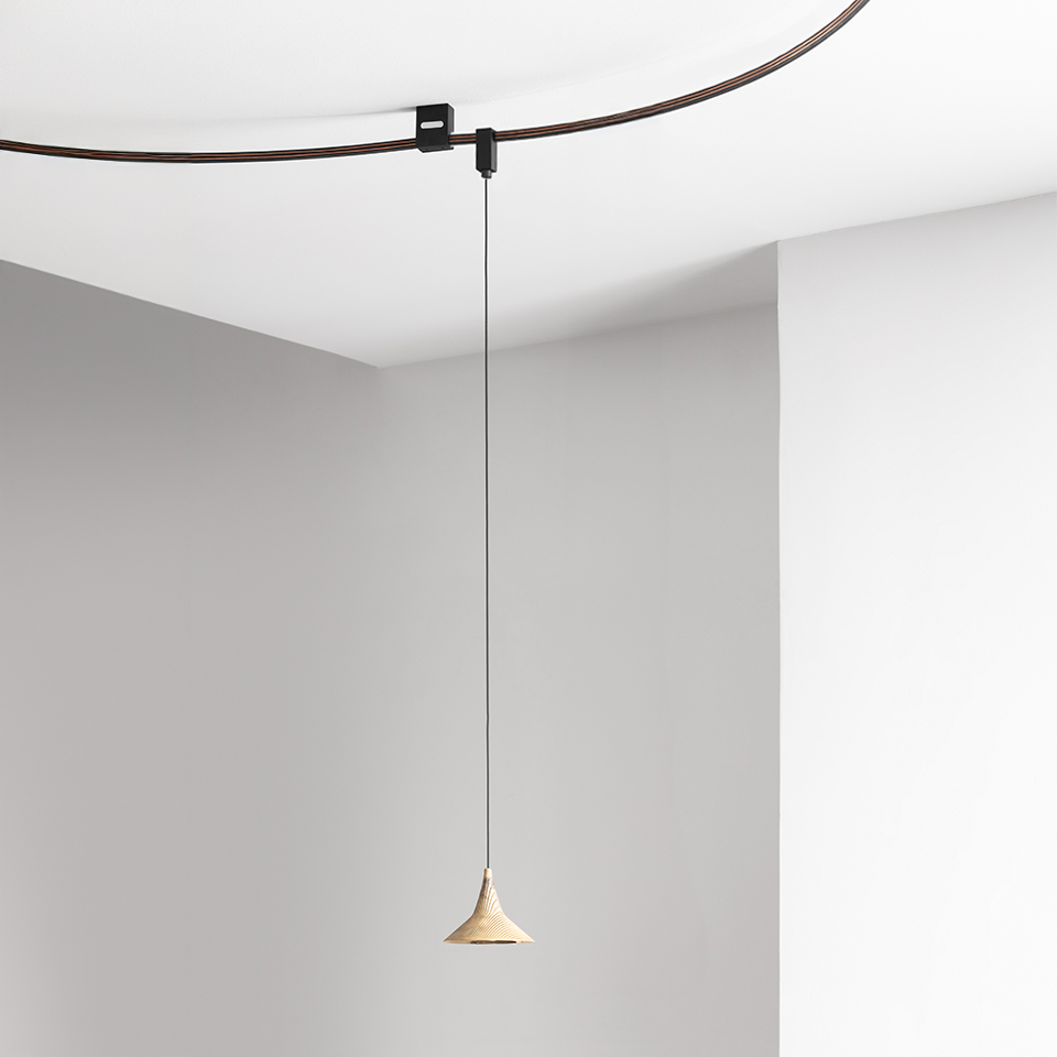 Artemide Sylt pendant lamp with small conical beige shade hanging from a thin cable on a curved dark ceiling track system