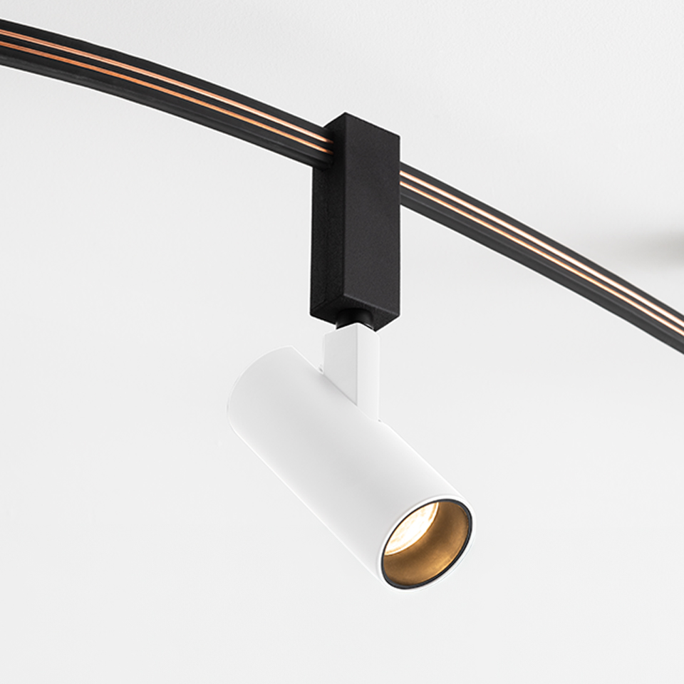 Artemide Sylt track spotlight: white cylindrical head with gold interior, mounted on a curved black track system via black adapter