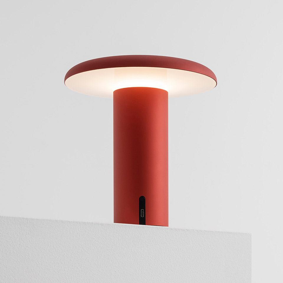 Artemide Takku portable table lamp in anodized red, mushroom-shaped diffuser on cylindrical stem with USB-C charging port