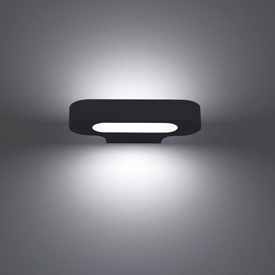 Talo wall lamp by Artemide: dark rectangular fixture with central oval LED strip emitting upward and downward light on wall