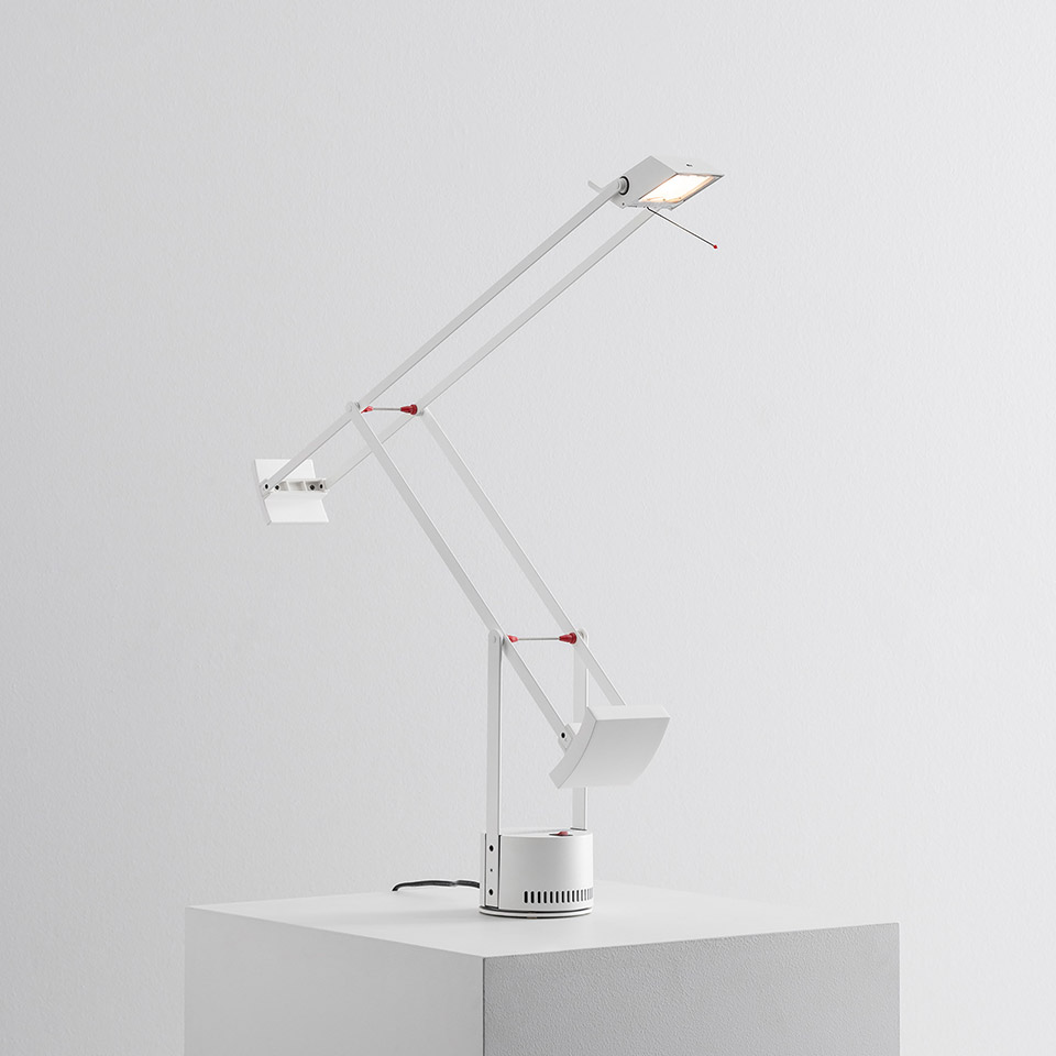 Artemide Tizio desk lamp in white with articulated arms, red joint accents, adjustable head, and circular base on white surface