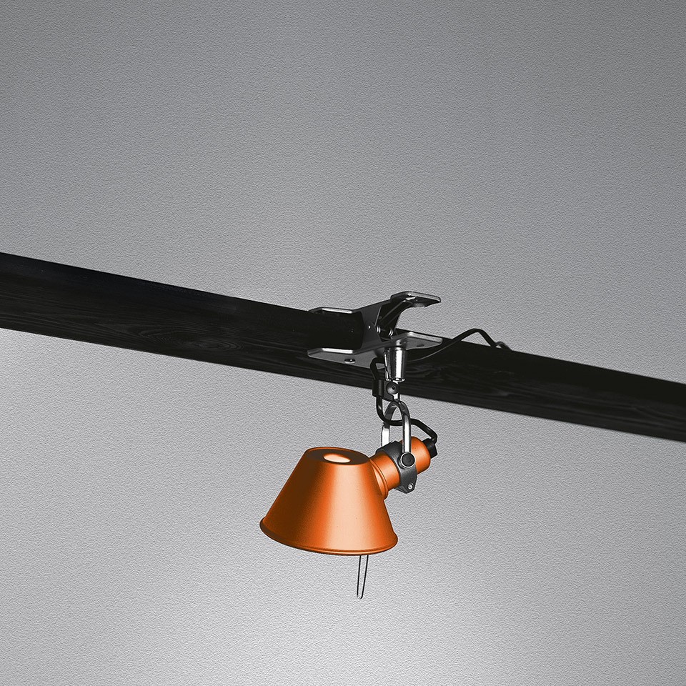 Artemide Tolomeo Pinza clip lamp in orange, clamped to a dark beam, with adjustable joint and conical shade pointing downward
