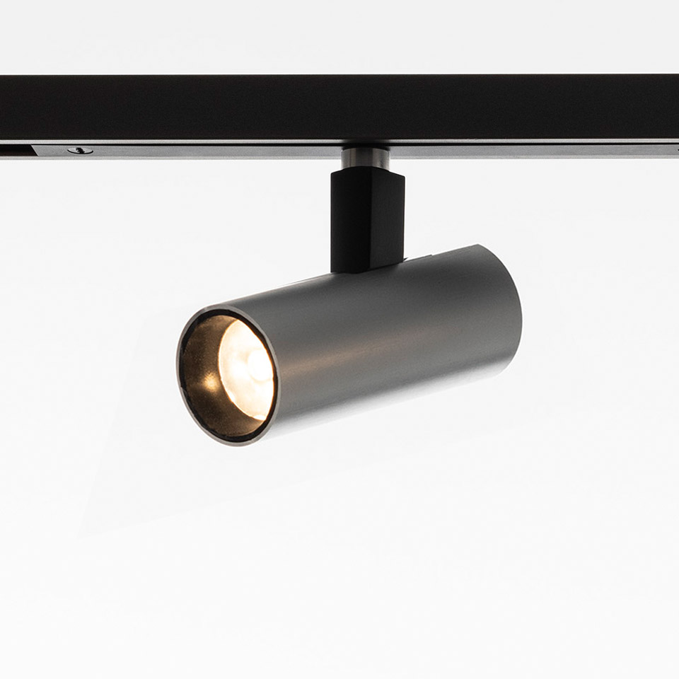 Artemide Turn Around System: cylindrical dark metal track spotlight mounted on black rail, emitting warm white light